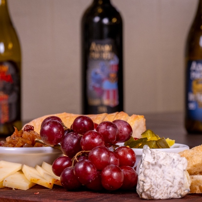 grapes, cheese and bread with 3 wine bottles in background